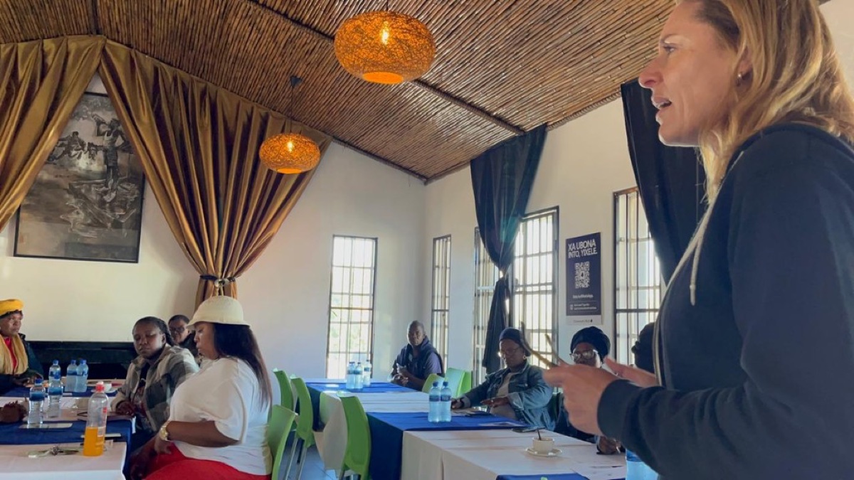 Gretha Groeneveld leading a community ambassador training session with residents seated at tables.
